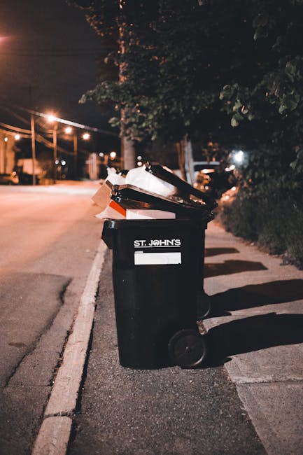 A large pile of black rubbish bags, many of which are tied at the top and appear full, are stacked against a modern building with a tiled exterior. Several light blue plastic water bottles are visibly